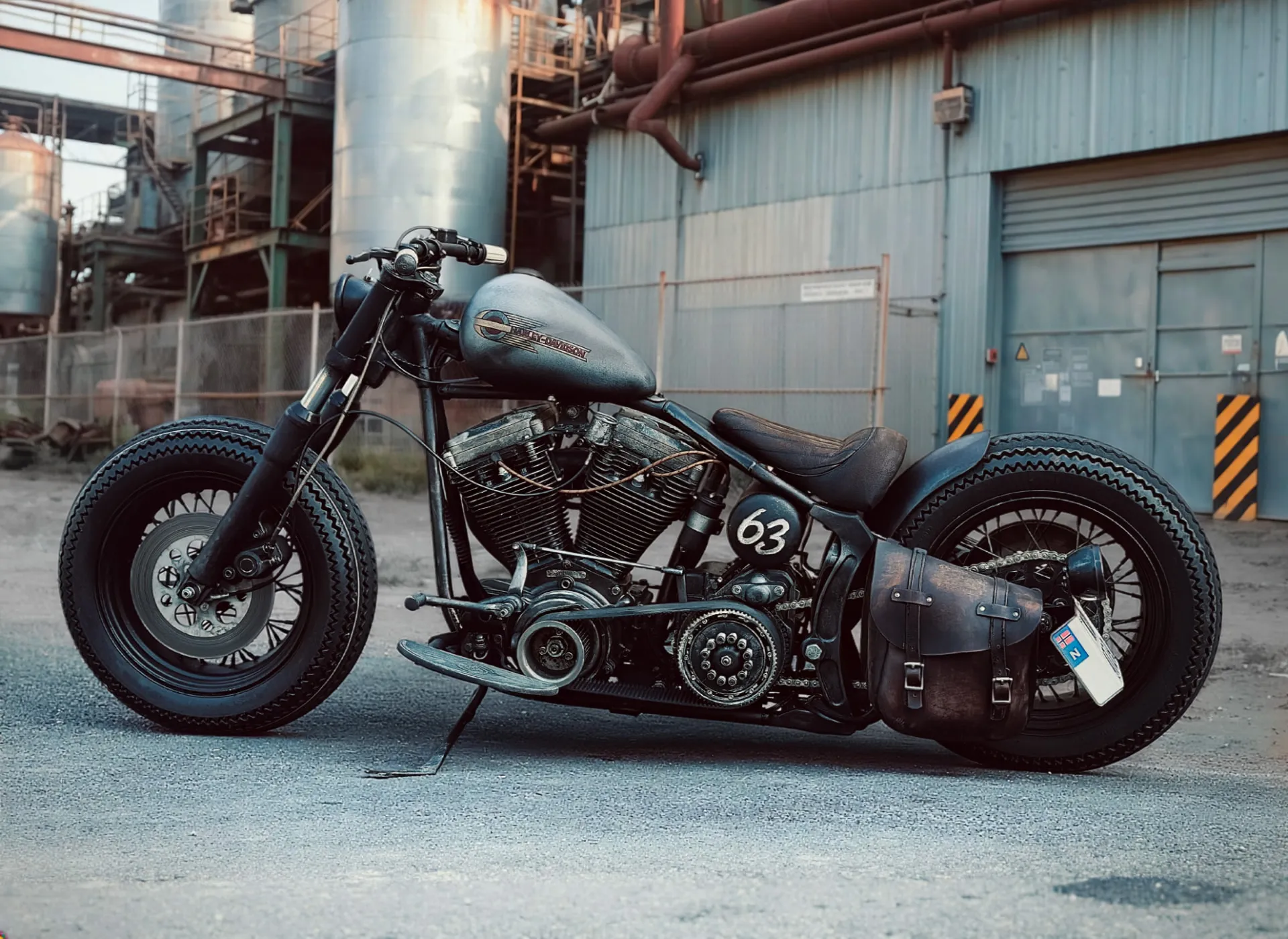 Jap Bobber custom motorcycle — a stripped-down bobber with number 63 side panel and leather saddlebag in an industrial yard.
