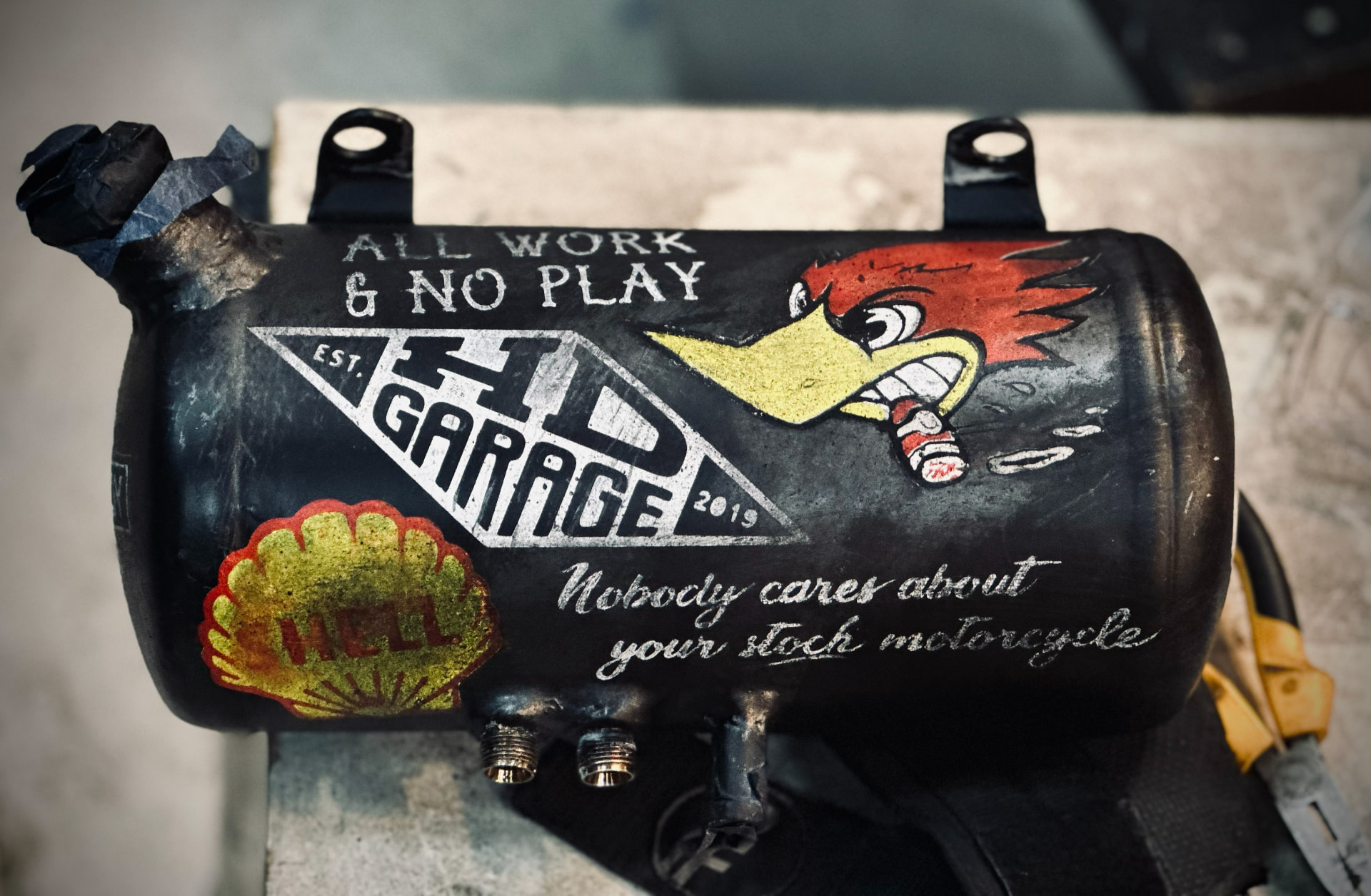 Hand-lettered oil tank reading All Work & No Play for HD Garage