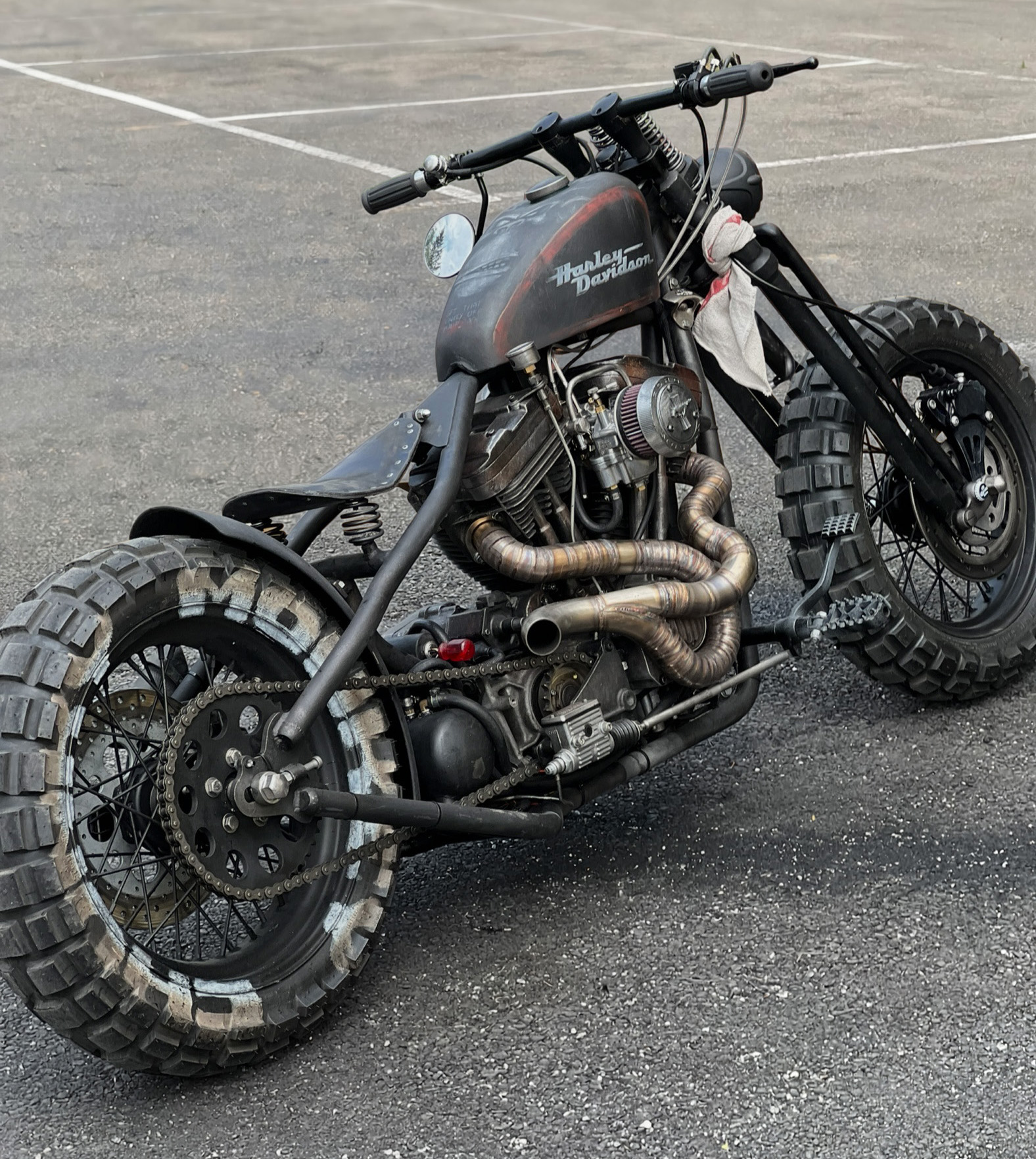 Custom Harley-Davidson bobber with knobby tyres and wrapped exhaust in a parking lot